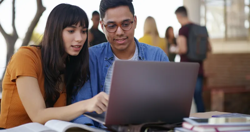 Dos postulantes de una academia preuniversitaria virtual revisando juntos un simulacro de admisión en su laptop
