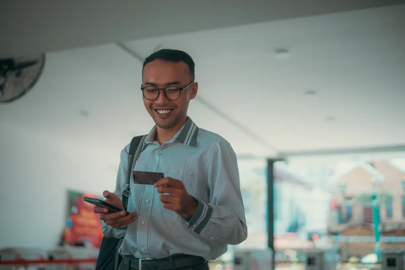 Emprendedor sonriente con su celular y una tarjeta en la mano revisando cómo cobrar cursos online con Yape y tarjeta