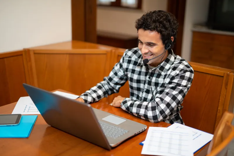 Coordinador académico con audífonos configurando en su laptop un aula virtual con Moodle, con hojas de planificación sobre la mesa