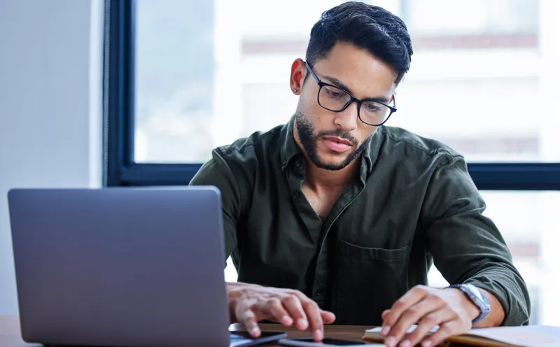 Coordinador académico con lentes organizando un curso en Moodle desde su laptop, con apuntes sobre el escritorio