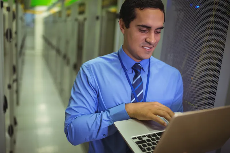 Técnico revisando en su laptop la copia de seguridad de Moodle dentro de una sala de servidores