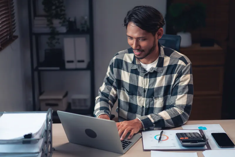 Director de un instituto comparando en su laptop las comisiones de Hotmart y de una pasarela de pagos, con calculadora y reportes de ventas