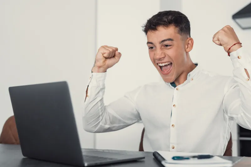Profesional joven celebrando frente a su laptop después de obtener una insignia digital por completar un curso
