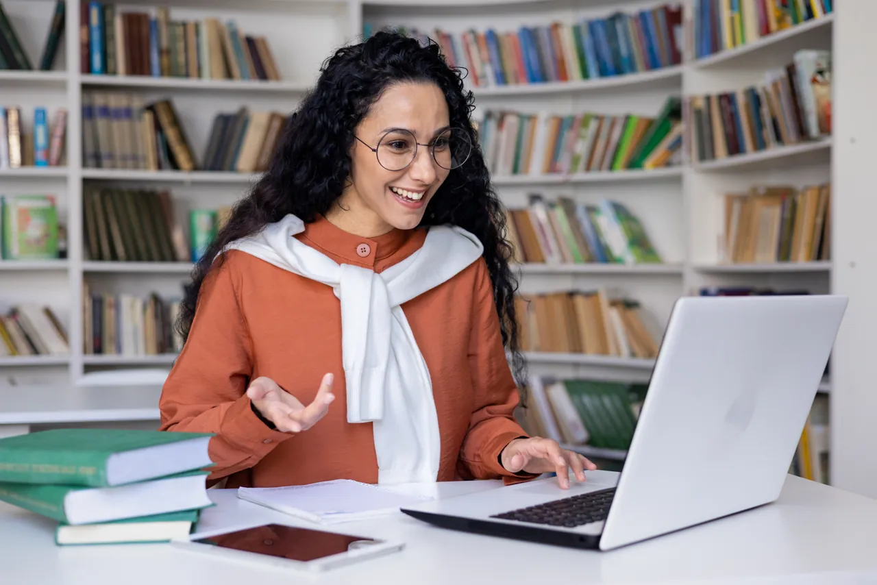 Estudiante de una maestría virtual participando en una clase en vivo desde su laptop, en una biblioteca
