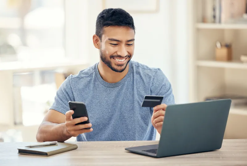 Hombre pagando un curso online con tarjeta desde su celular frente a la laptop, en una pasarela de pagos peruana