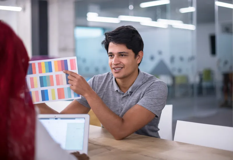 Coordinador de un instituto muestra una paleta de colores de la marca para personalizar Moodle, frente a una laptop