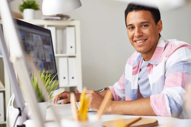 Diseñador sonriente en su escritorio preparando en la computadora la plantilla de certificado de curso de un instituto