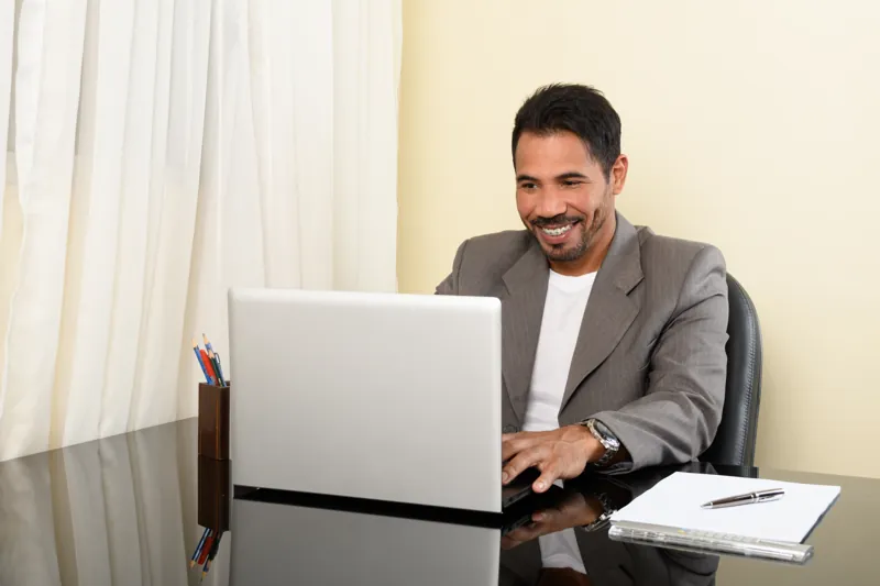 Director de un instituto sonriendo frente a su laptop mientras revisa el precio del dominio .pe y el hosting de su web
