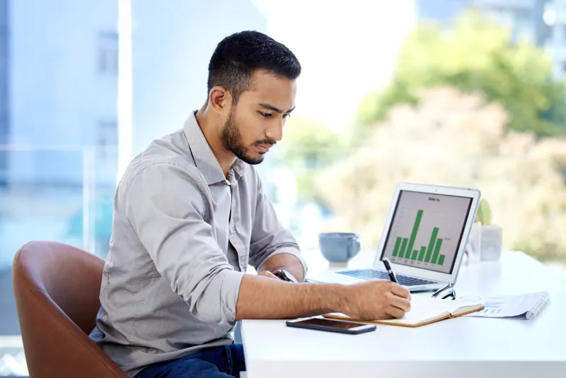 Responsable de marketing de una academia anotando datos de posicionamiento en Google junto a su laptop con gráficos de visitas