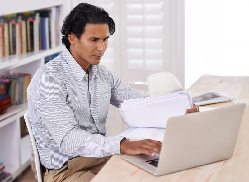 Director de un instituto revisando reportes de notas y pagos en su laptop, con documentos sobre el escritorio