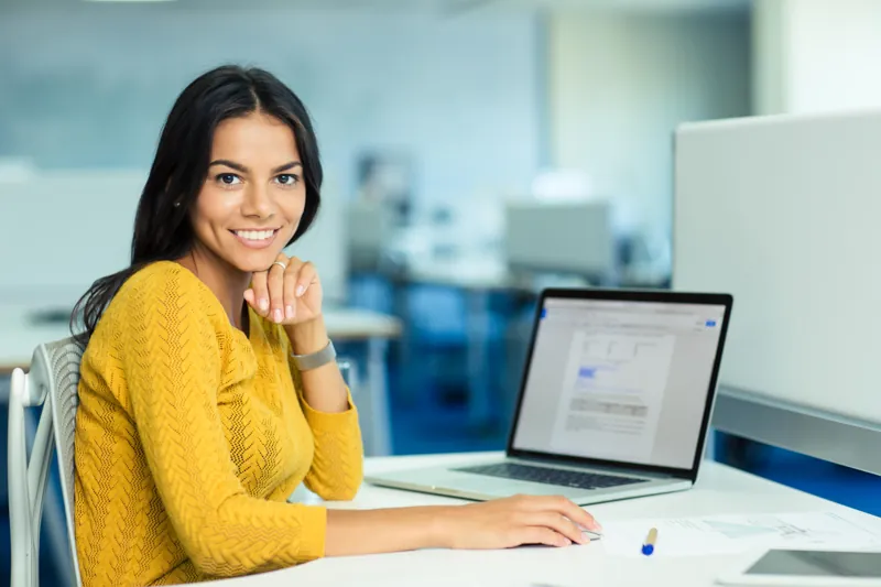Coordinadora de un instituto sonriendo frente a su laptop, donde revisa las matrículas online del nuevo ciclo