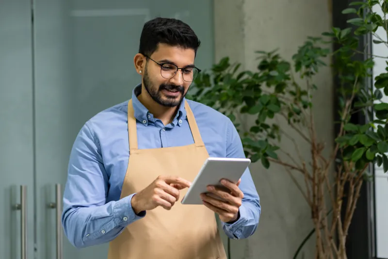 Dueño de un pequeño negocio con delantal revisando pedidos en una tablet, como primer paso de la transformación digital de su pyme