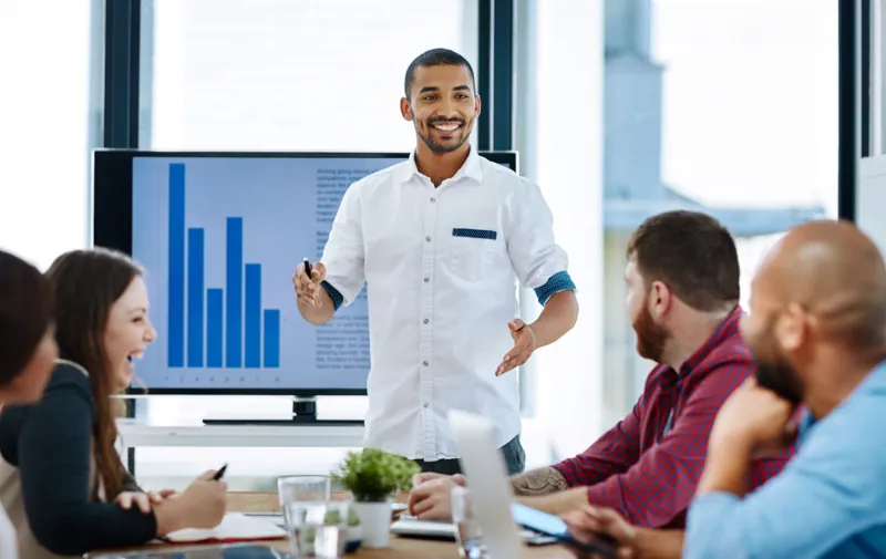 Consultor presentando a un equipo de una empresa su propuesta de cursos de capacitación con gráficos en pantalla