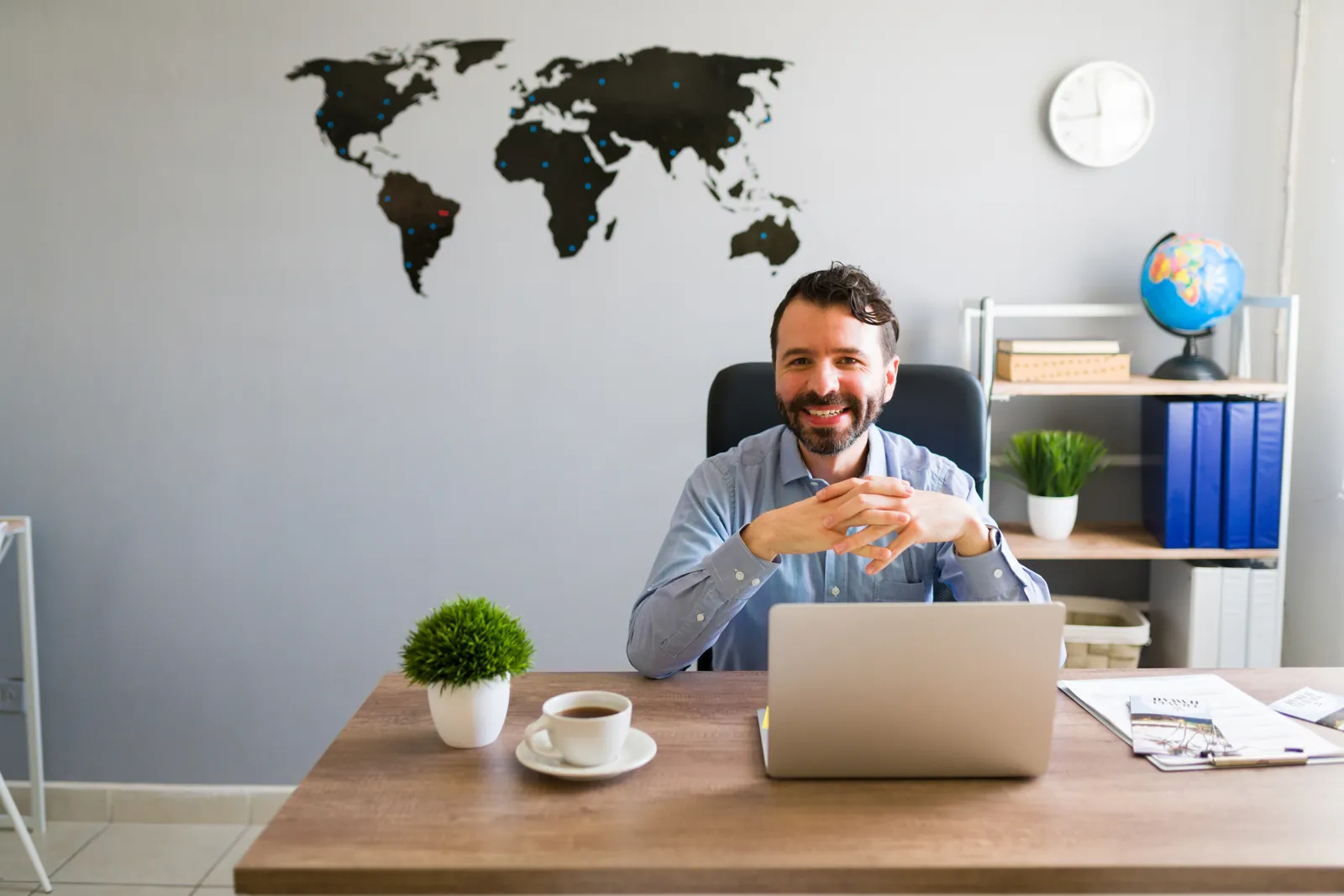 Director de un centro de capacitación en su oficina con un mapa del mundo detrás, listo para vender cursos al extranjero