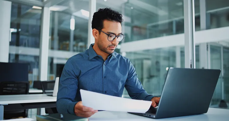Responsable de recursos humanos revisando un certificado impreso y comprobándolo en el verificador de certificados desde su laptop